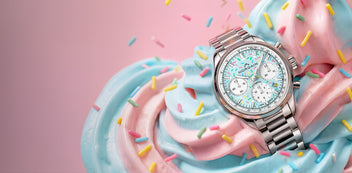 Watch with a colorful face on top of a pink and blue whipped cream dessert with sprinkles.